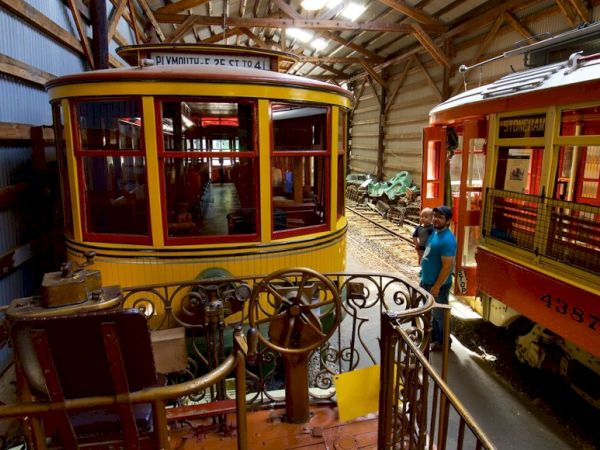 The image shows vintage trolley cars in a museum setting, with a person holding a child nearby for close viewing.