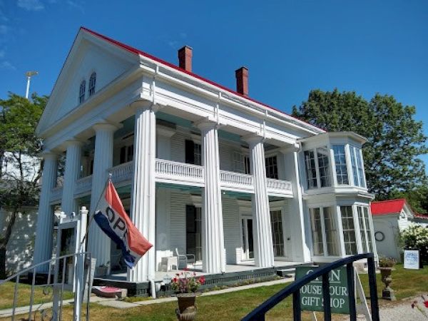 The image shows a large white historic building with columns, an "OPEN" flag, and signs for a house tour and gift shop.