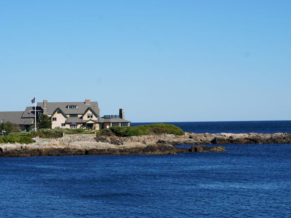A house on a rocky coastline with greenery, a flagpole, and a clear blue sky above the ocean.