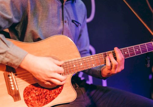 A person is playing an acoustic guitar, focusing on strumming and fretwork, under stage lighting.