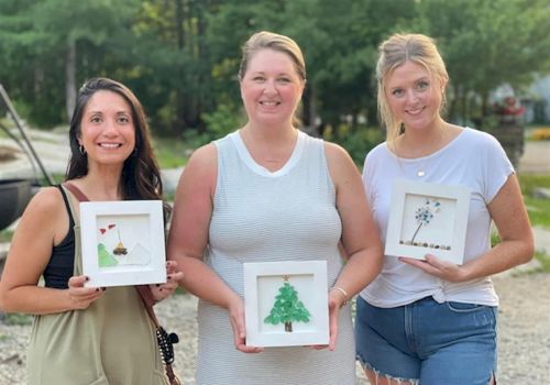 Three people outdoors holding framed art with small tree and nature designs.