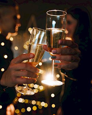 People toasting with champagne glasses, creating a celebratory atmosphere with warm, blurry lights in the background.